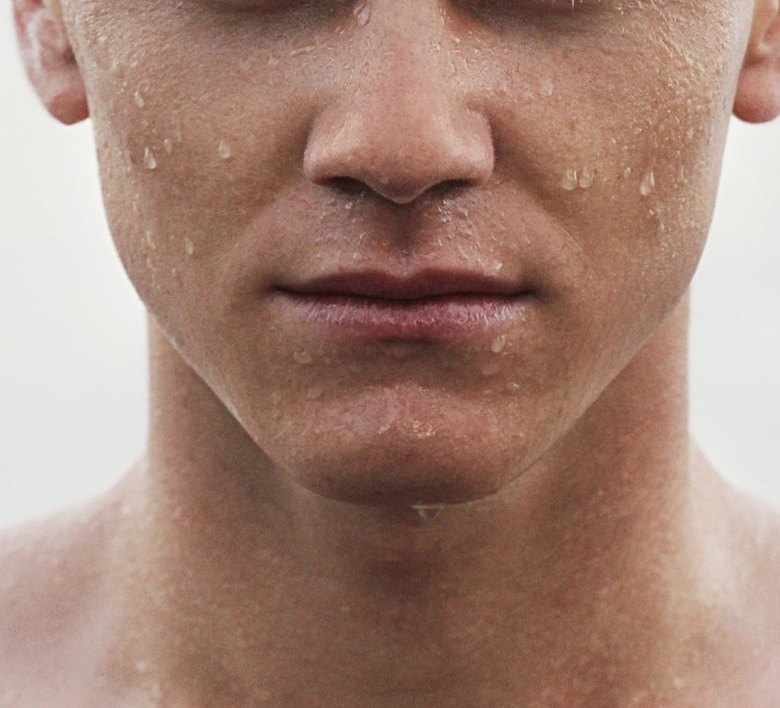 The lower half of someone's face with a strong jawline, with beads of water on the skin.